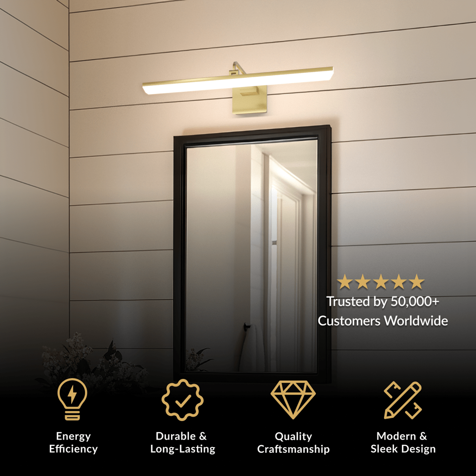 Zena bathroom light in brushed gold, slim horizontal bar mounted above a black-framed mirror on a dark wall
