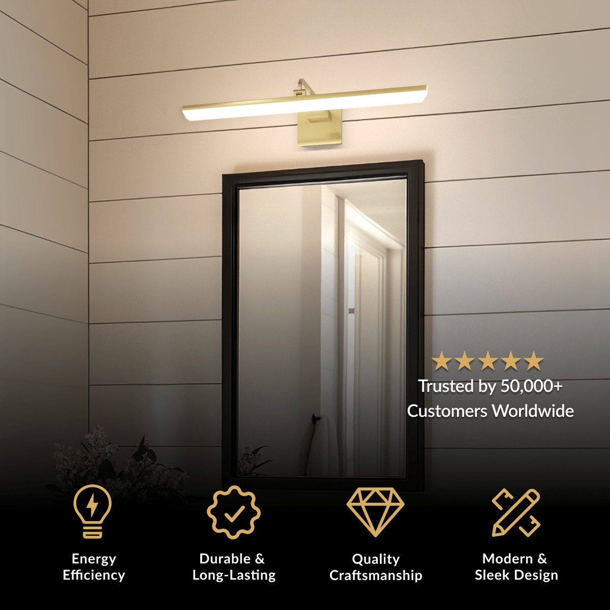 Zena bathroom light in brushed gold, slim horizontal bar mounted above a black-framed mirror on a dark wall