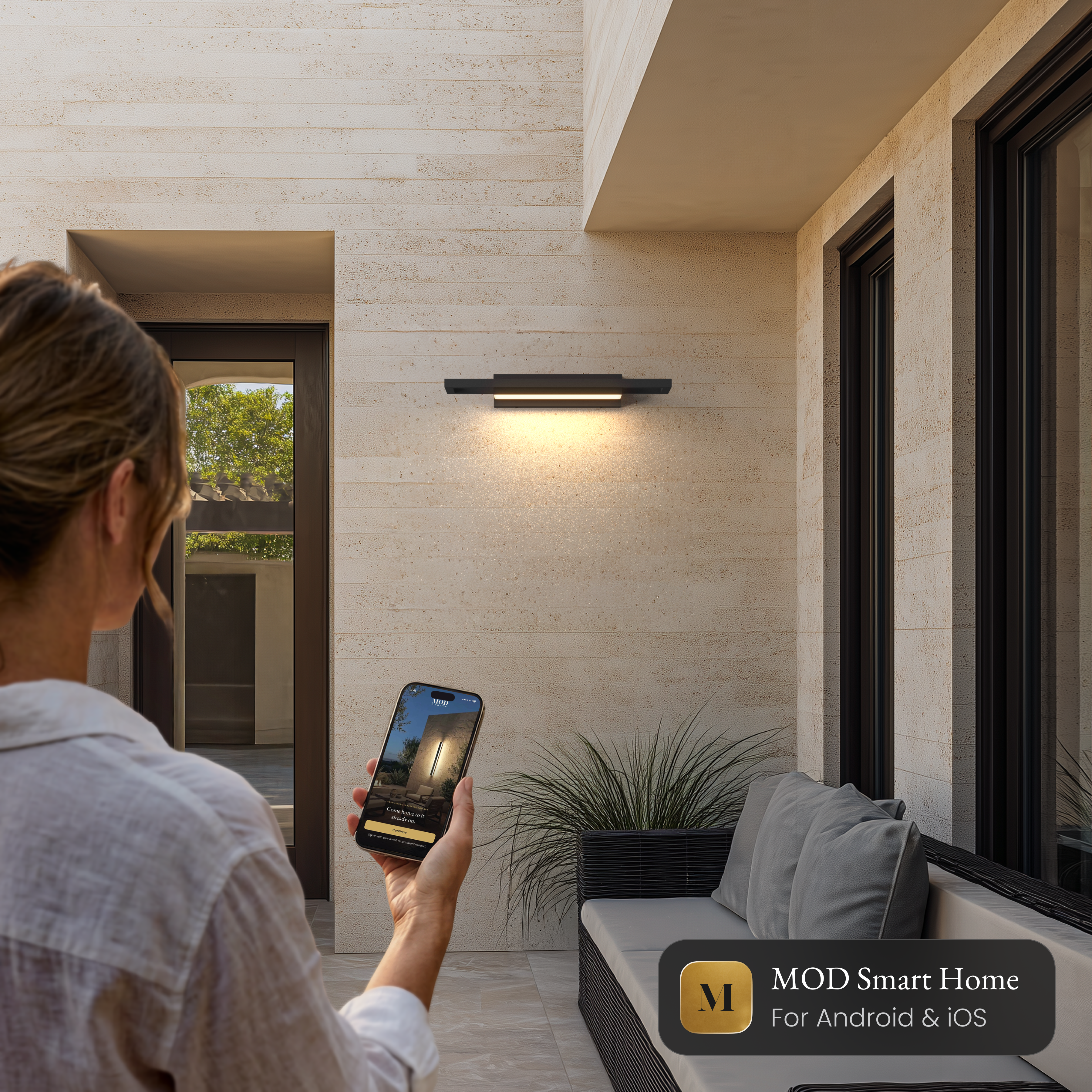Brooklyn Smart black stainless outdoor sconce on a stone wall, controlled from the MOD Smart Home app on a phone