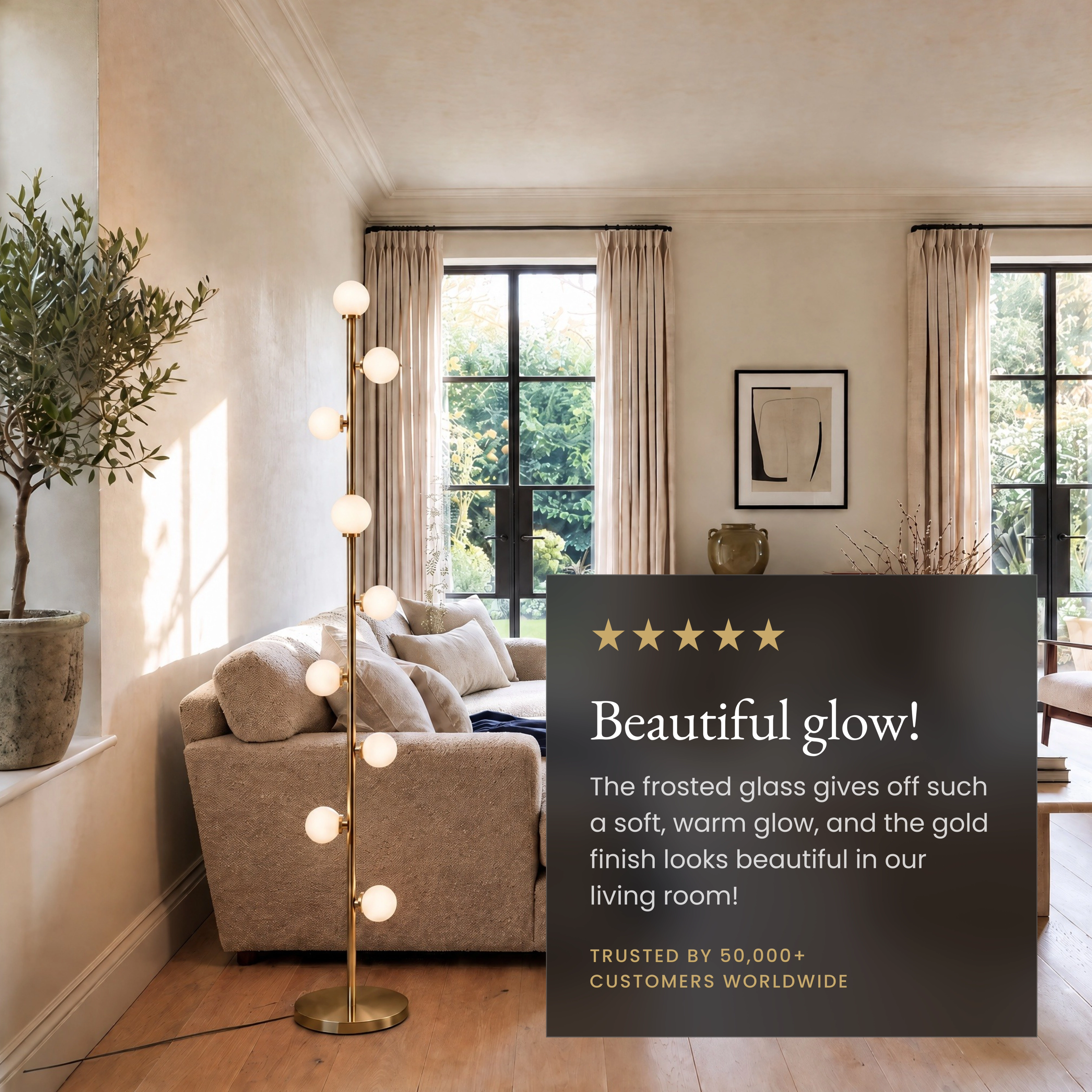 Pearl floor lamp in gold beside a grey armchair in a living room; frosted glass globes stacked on a slim metal stem