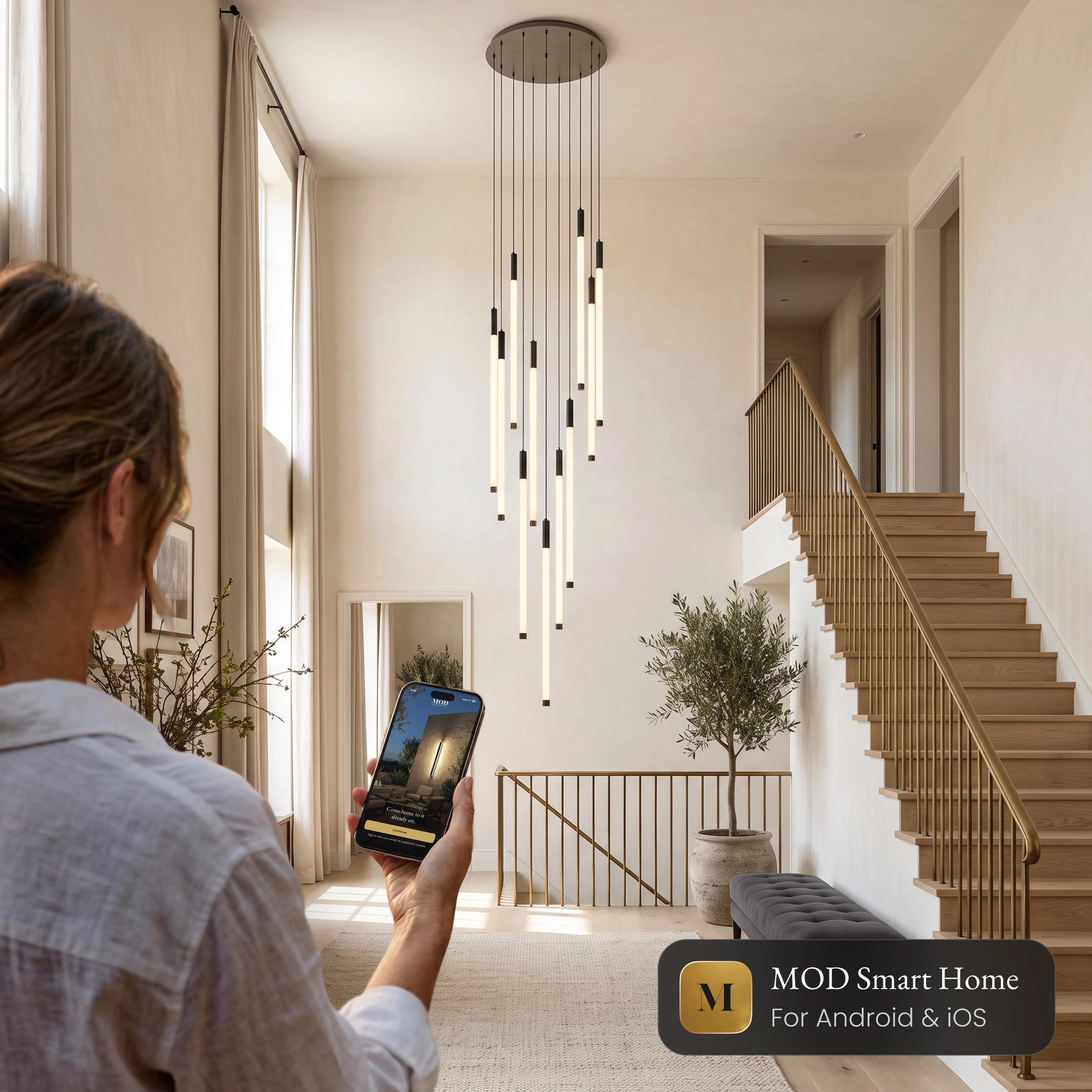 Woman controlling the Kasper Smart staircase chandelier from the MOD Smart Home app on her phone
