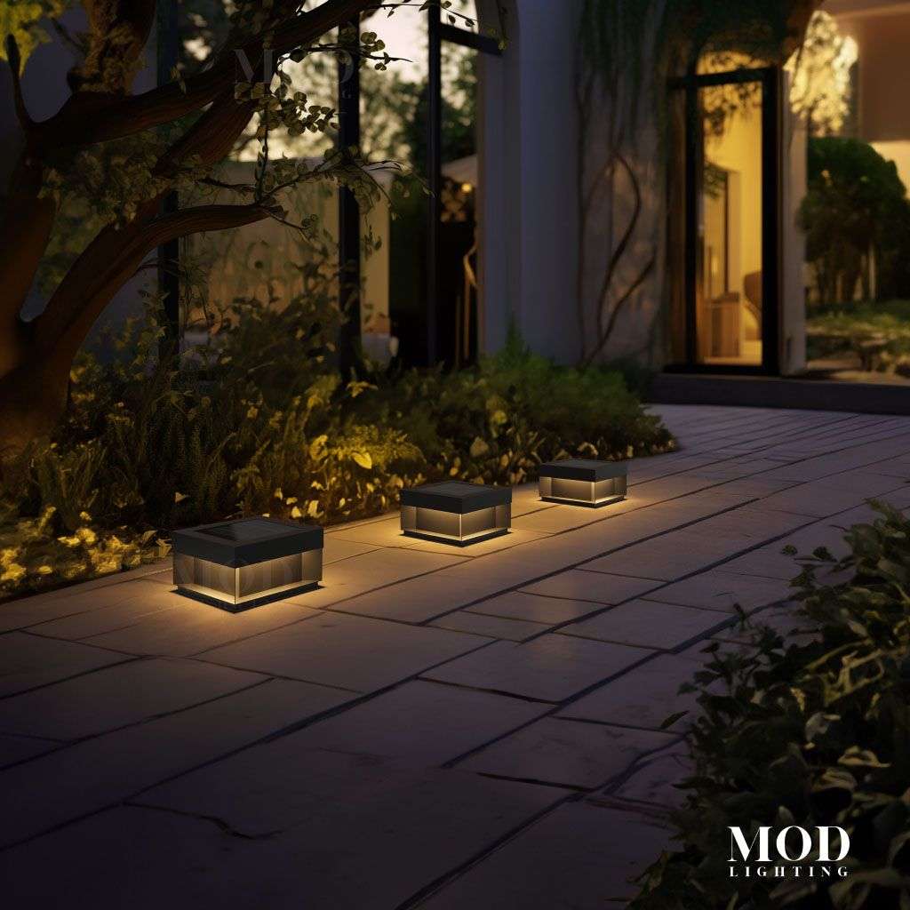 Chaz three warm-glowing solar bollard path lights on a paved garden walkway at night