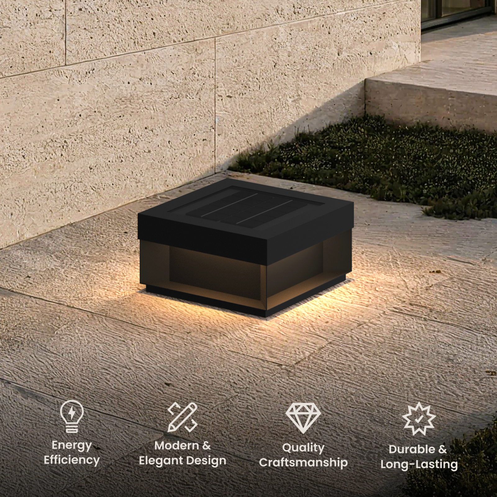 Chaz solar lamp, low square black bollard with warm glow, on a stone patio beside a wall