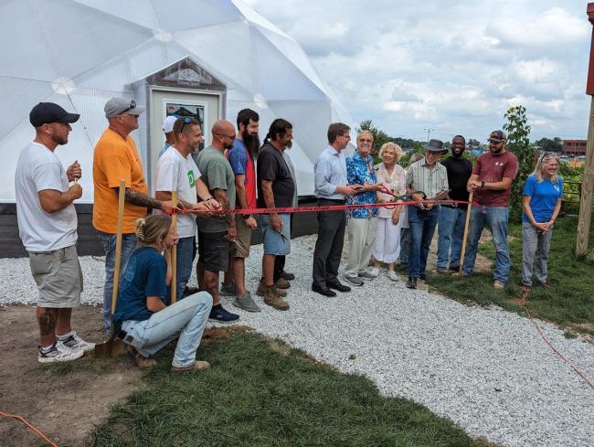 Community members gathered outside a Growing Dome greenhouse during a ribbon cutting event.