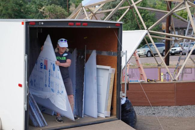 woman unloading polycarbonate triangles from a trailer with a greenhouse under construction in the background