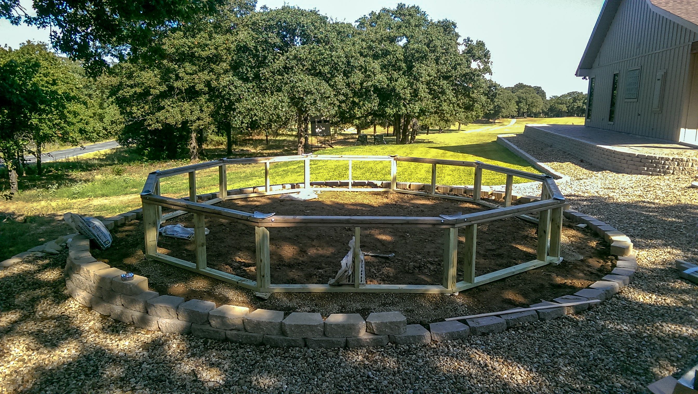foundation wall of a greenhouse being installed on a beautiful site located close to the house with deciduous trees