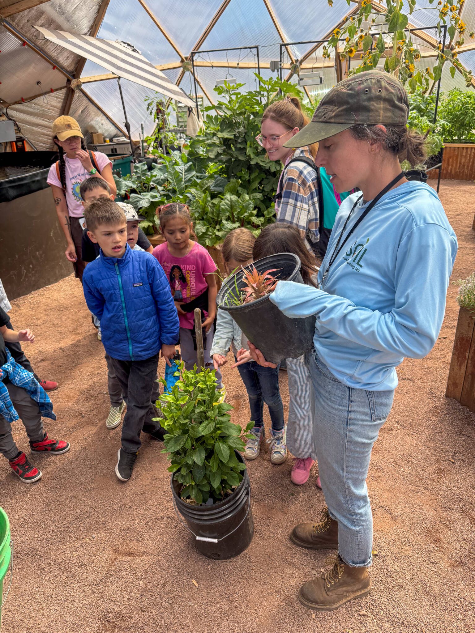 Teacher showing young students a pineapple plant and a lemon tree in a Growing Dome