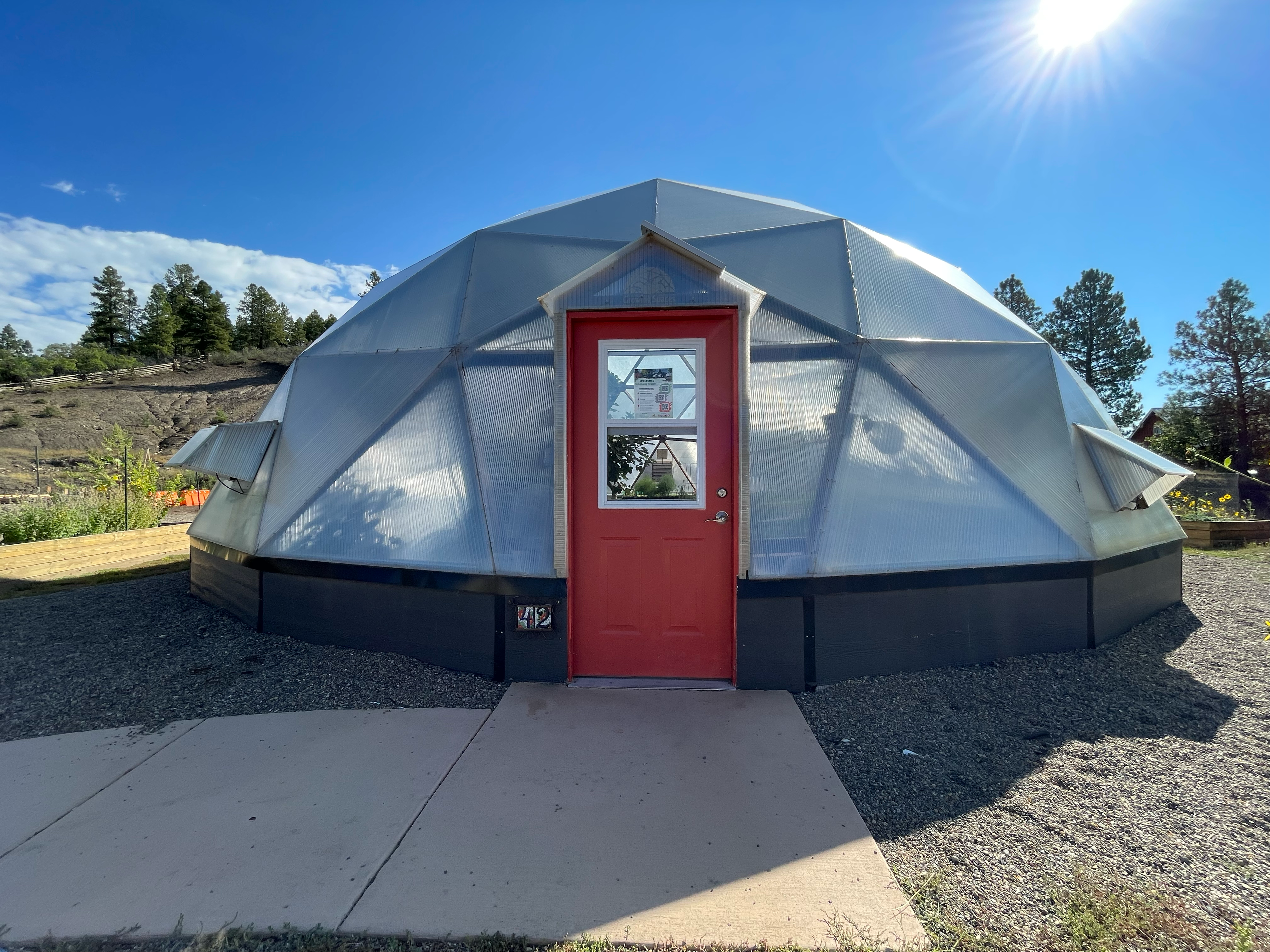 42' Growing Dome with a red door and the sun behind it illuminating the structure