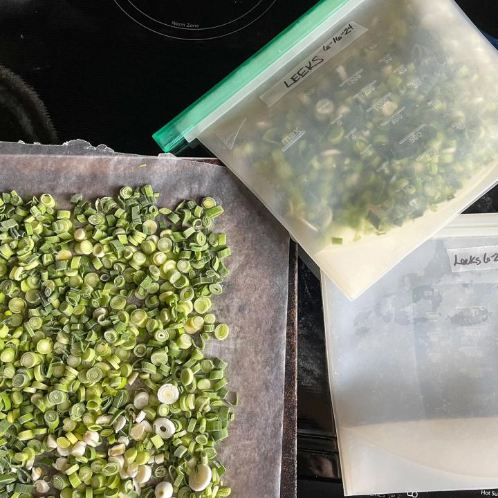 chopped and frozen leeks on a cookie sheet lined with wax paper and silicone bags filled with frozen leeks