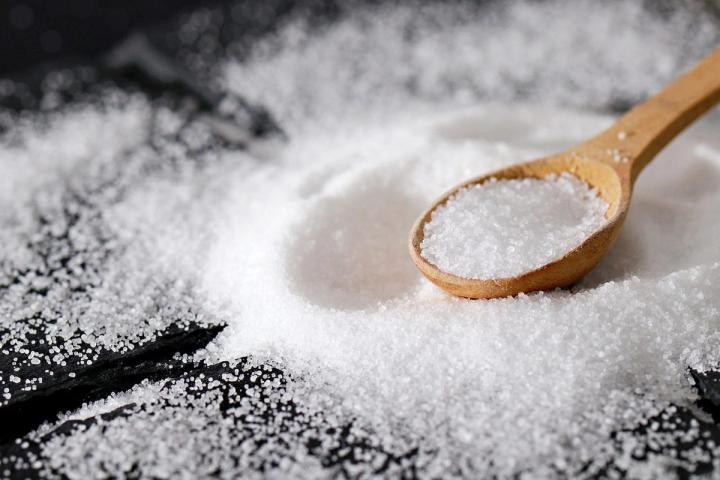 well of salt on a dark surface with a wooden spoon sitting in the pile of salt