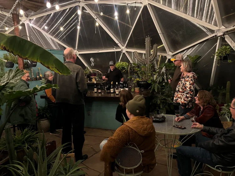 People gathered around a table and bar inside a Growing Dome greenhouse at night