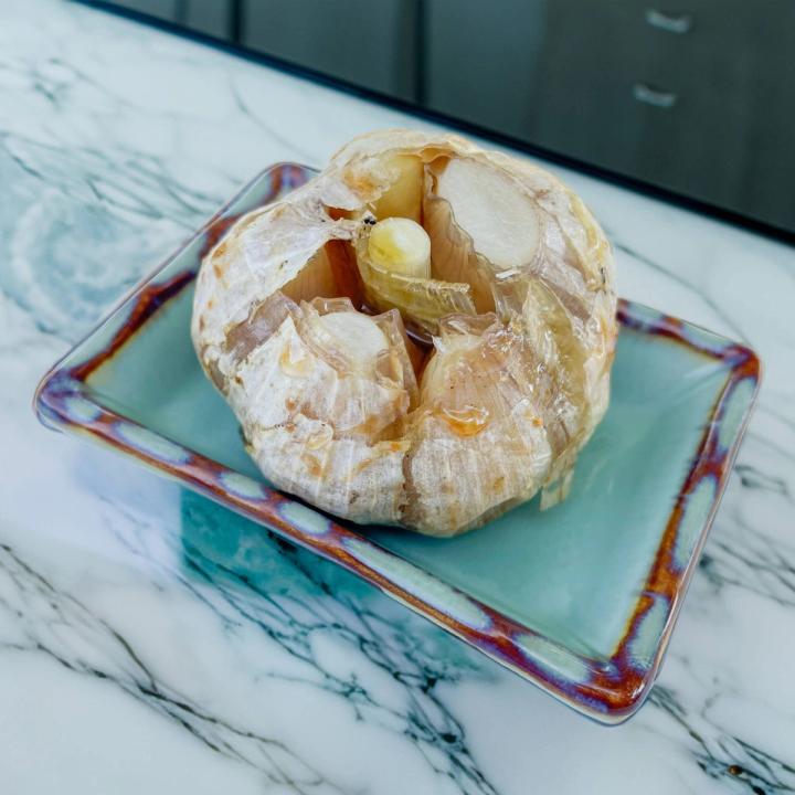 head of roasted garlic sitting in a small green dish on a marble countertop
