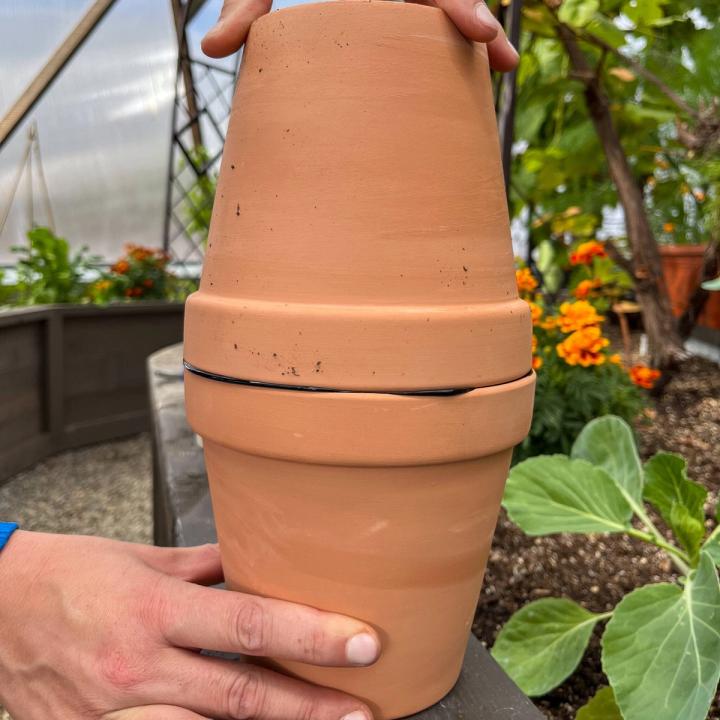 Two terracotta pots being attached to each other with waterproof silicone. One upright and the other inverted to make a large reservoir to hold water.