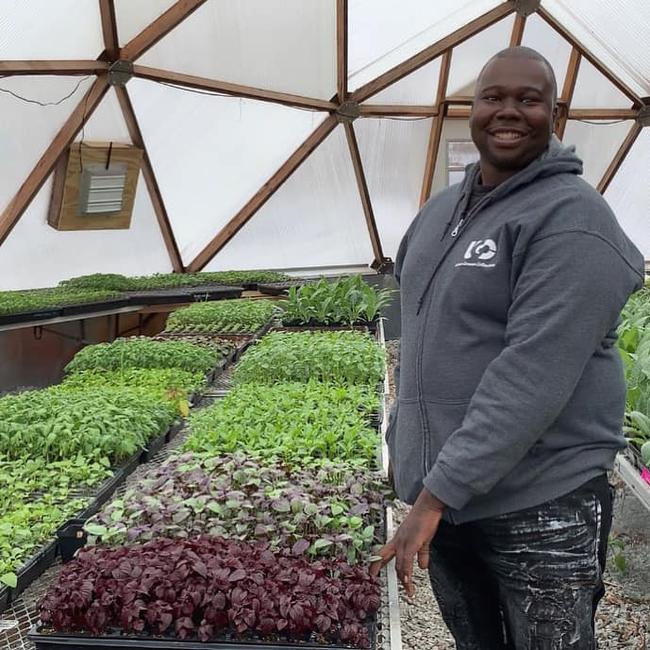 Farmer from the Urban Growers Initiative standing inside a large Growing Dome greenhouse with rows of leafy green seedlings.