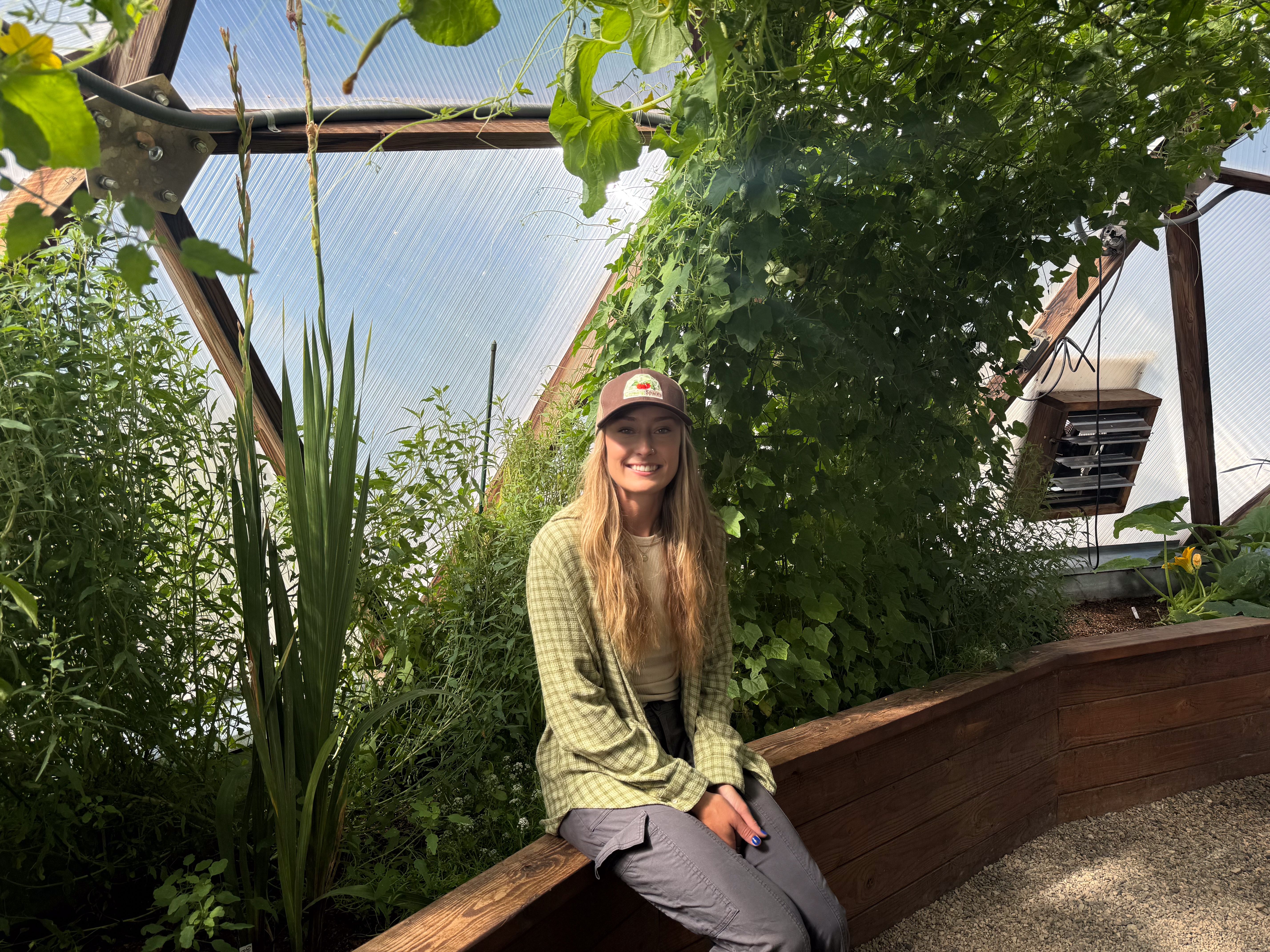 Person wearing a brown hat seated on a greenhouse raised bed