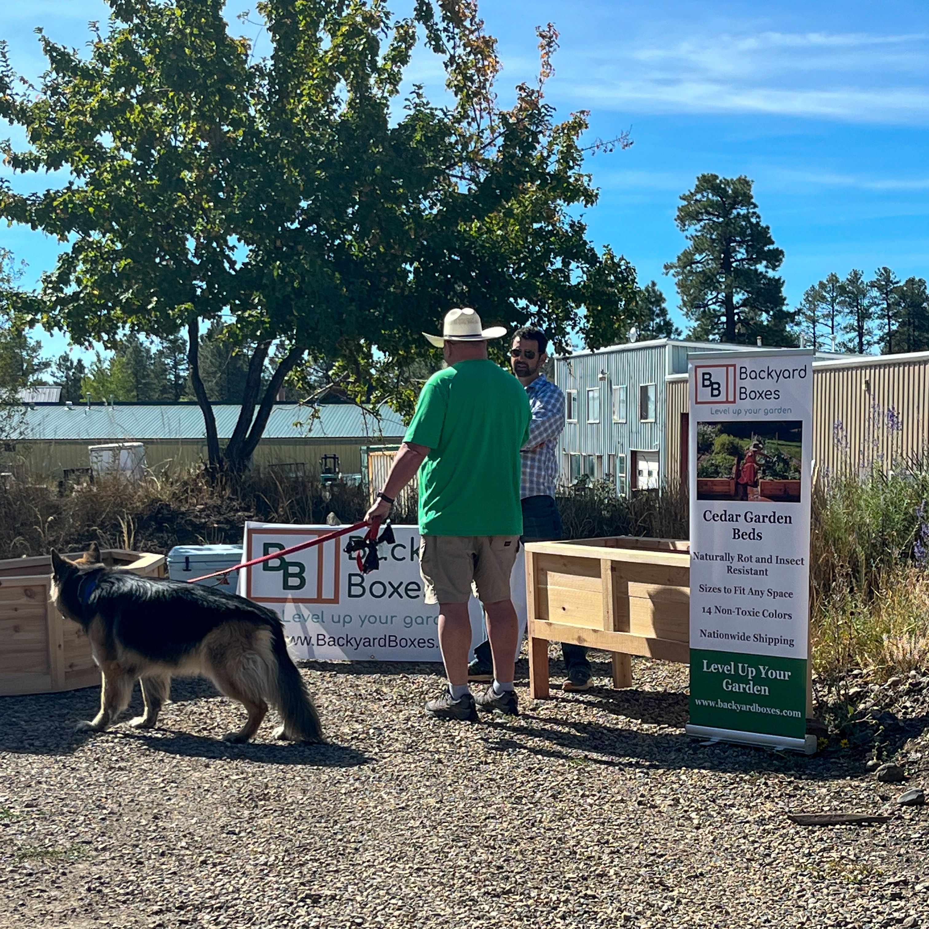 Two men and a dog talking about garden beds at a gardening event