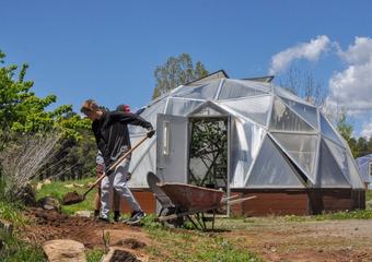 Two young men shoveling soil from a hillside into a wheelbarrow with a growing dome in background
