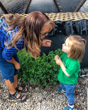 a woman holding a leaf showing it to a child as they stand inside a greenhouse