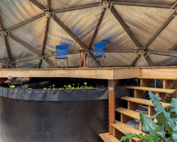 two blue camping chairs sitting atop a deck built above the above ground pond in a 42' Growing Dome