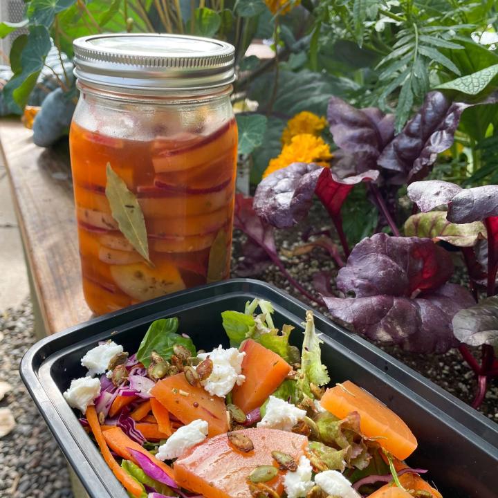 jar of pickled beets sitting on a raised bed in a greenhouse with salad in the foreground and beets growing in the background