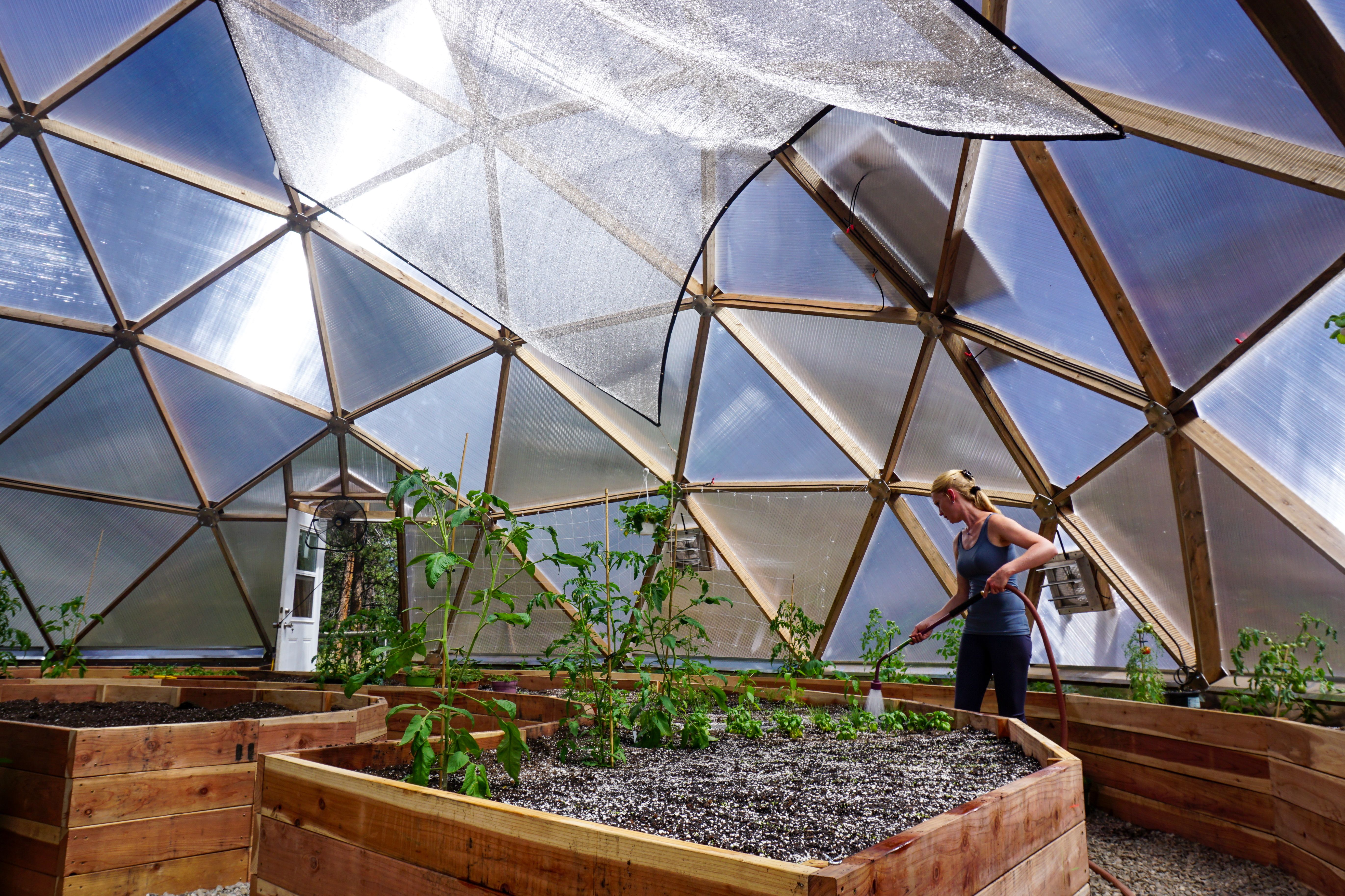woman watering raised beds inside of a growing dome