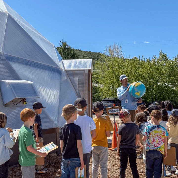 Teacher demonstrating how the sun moves across the sky with a globe outside a growing dome greenhouse