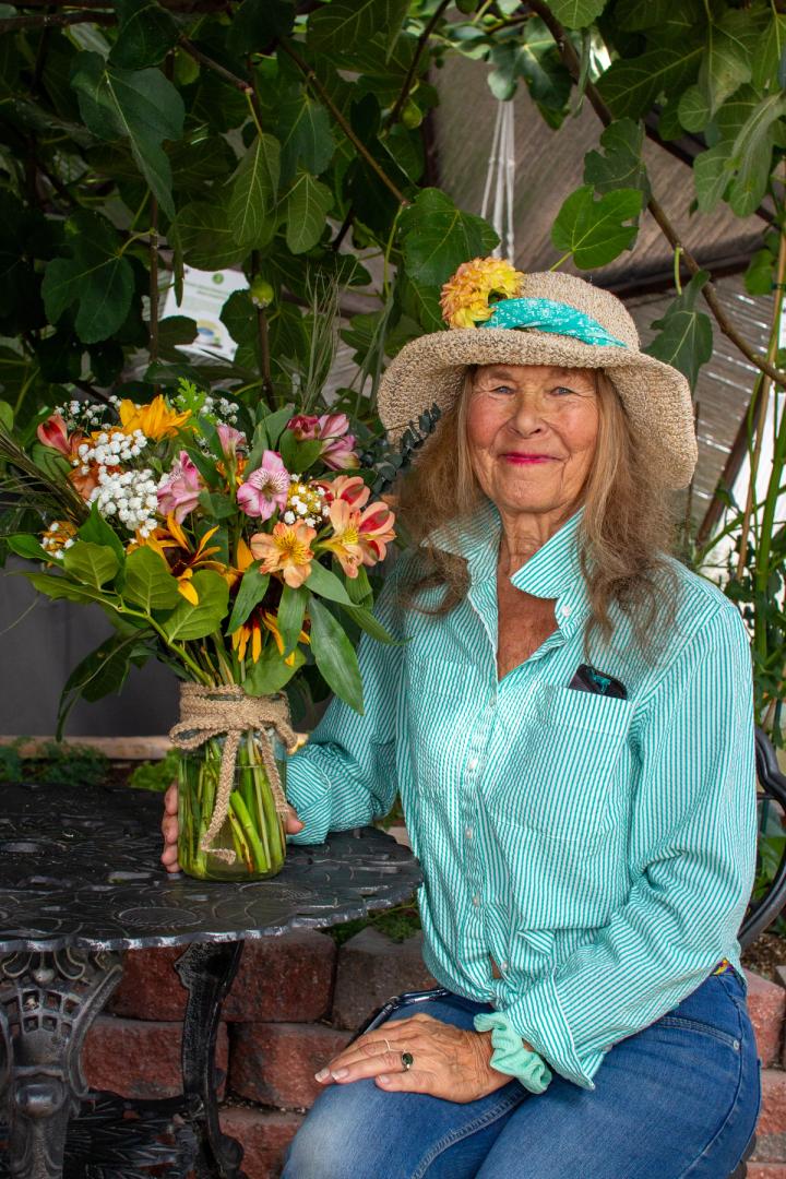 Woman in a bright blue shirt and straw hat holding a handmade bouquet