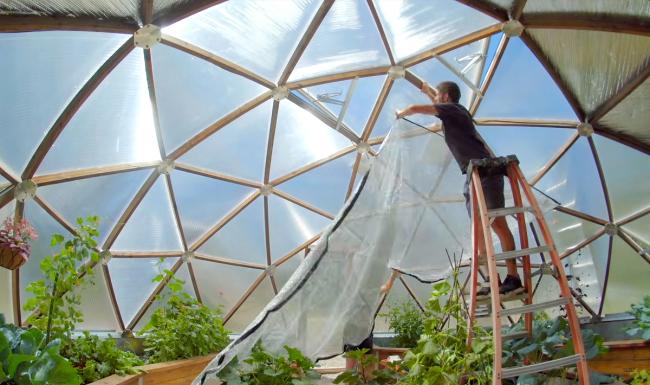 Person installing reflective shade cloth inside a Growing Dome greenhouse