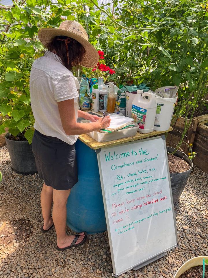 Gardener writing daily notes in a shared notebook standing next to a sign detailing what can be harvested