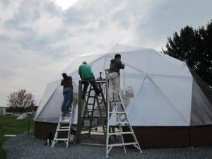 Volunteers installing polycarbonate glazing to greenhouse doorway