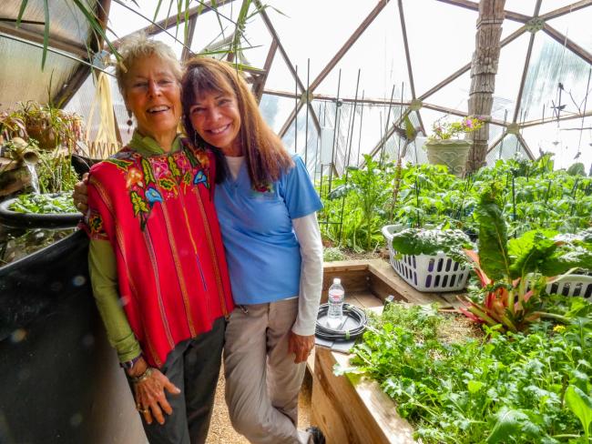 Two women smiling at the camera inside a Growing Dome geodesic greenhouse