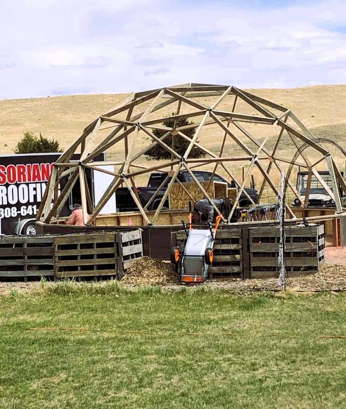 Two men attaching large sheets of metal together in a geodesic greenhouse