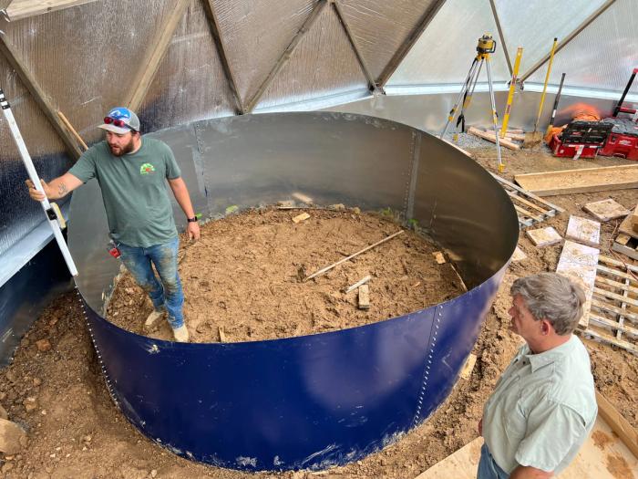 Growing spaces supervisor leveling a pond in a growing dome while the owner watches