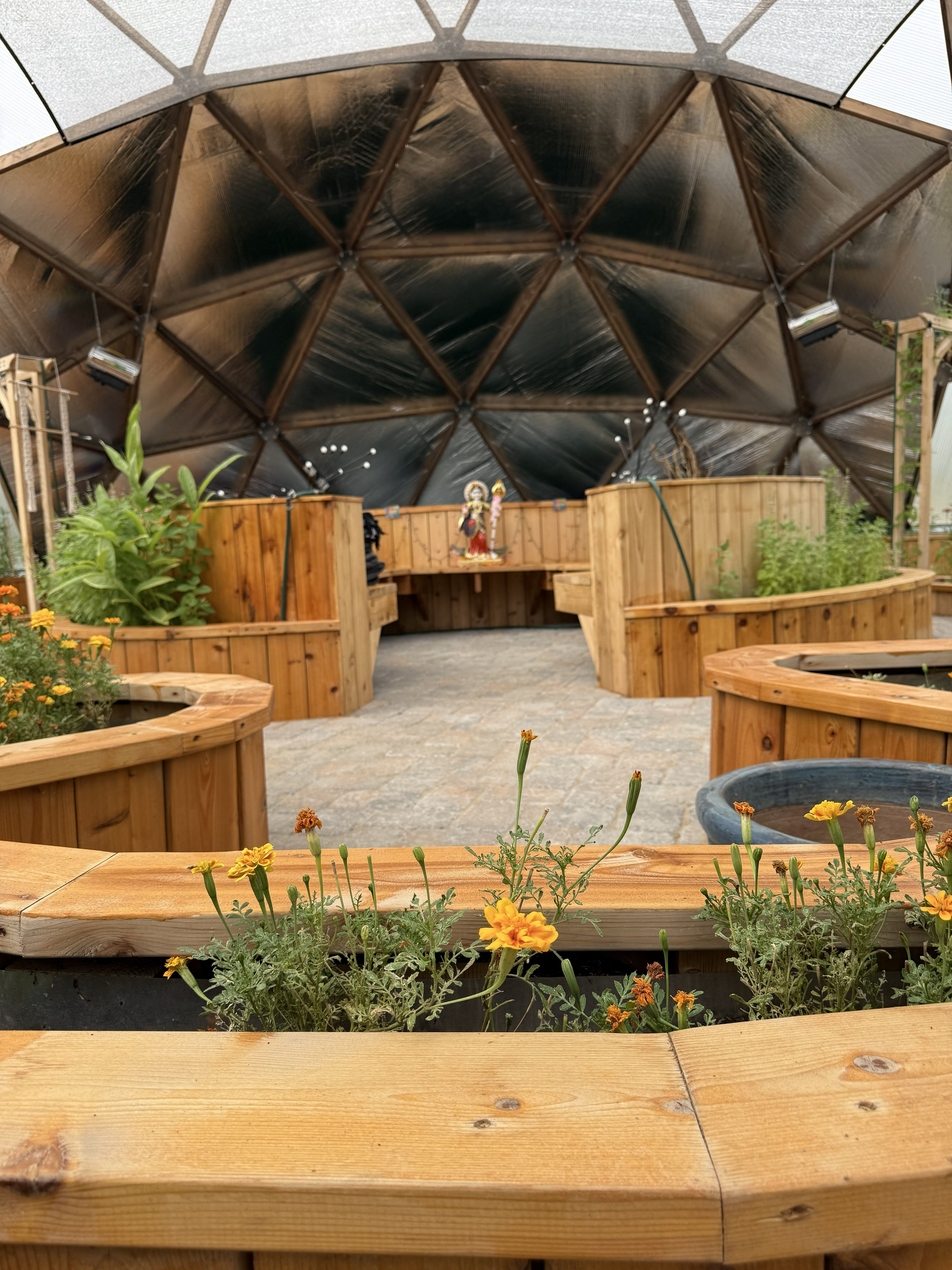 geodesic dome interior at Kula Kamala facing the north wall with marigolds in foreground and a statue on a bench near the pond area