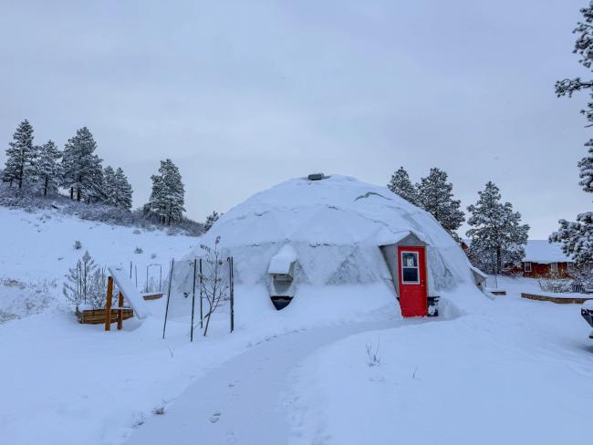 42 foot diameter growing dome with red door covered in a light layer of snow