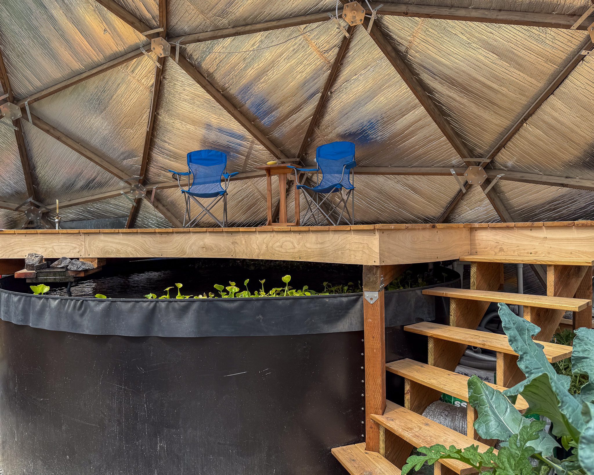 two blue camping chairs sitting atop a deck built above the above ground pond in a 42' Growing Dome