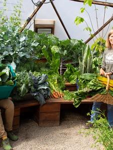 two women surrounded by a large vegetable garden harvest in a 42 foot diameter growing dome greenhouse