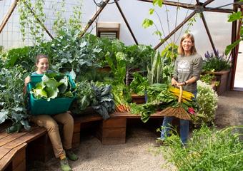 two women surrounded by a large vegetable garden harvest in a 42 foot diameter growing dome greenhouse