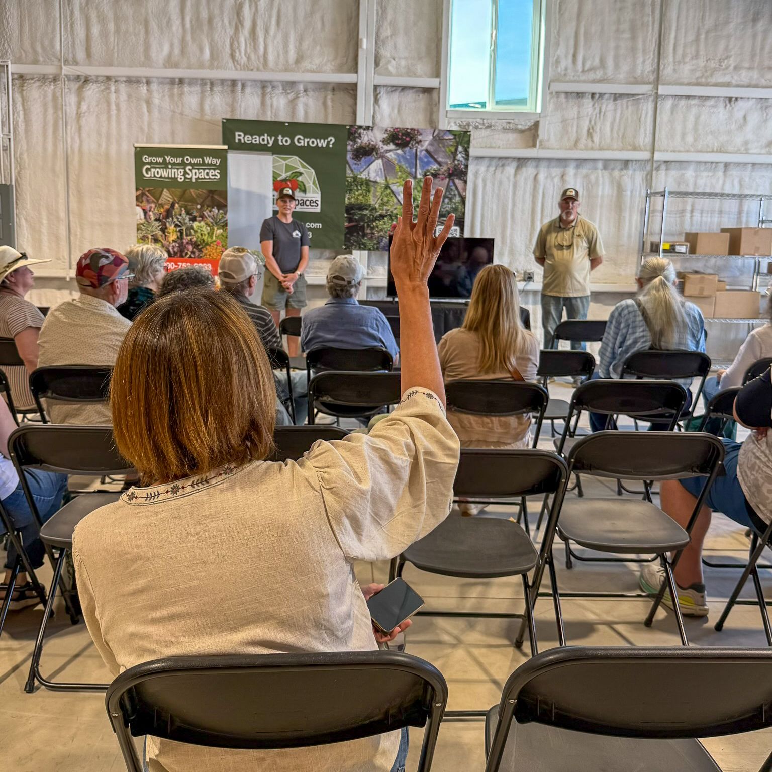 A person seated in a class setting with their hand raised to pose a question