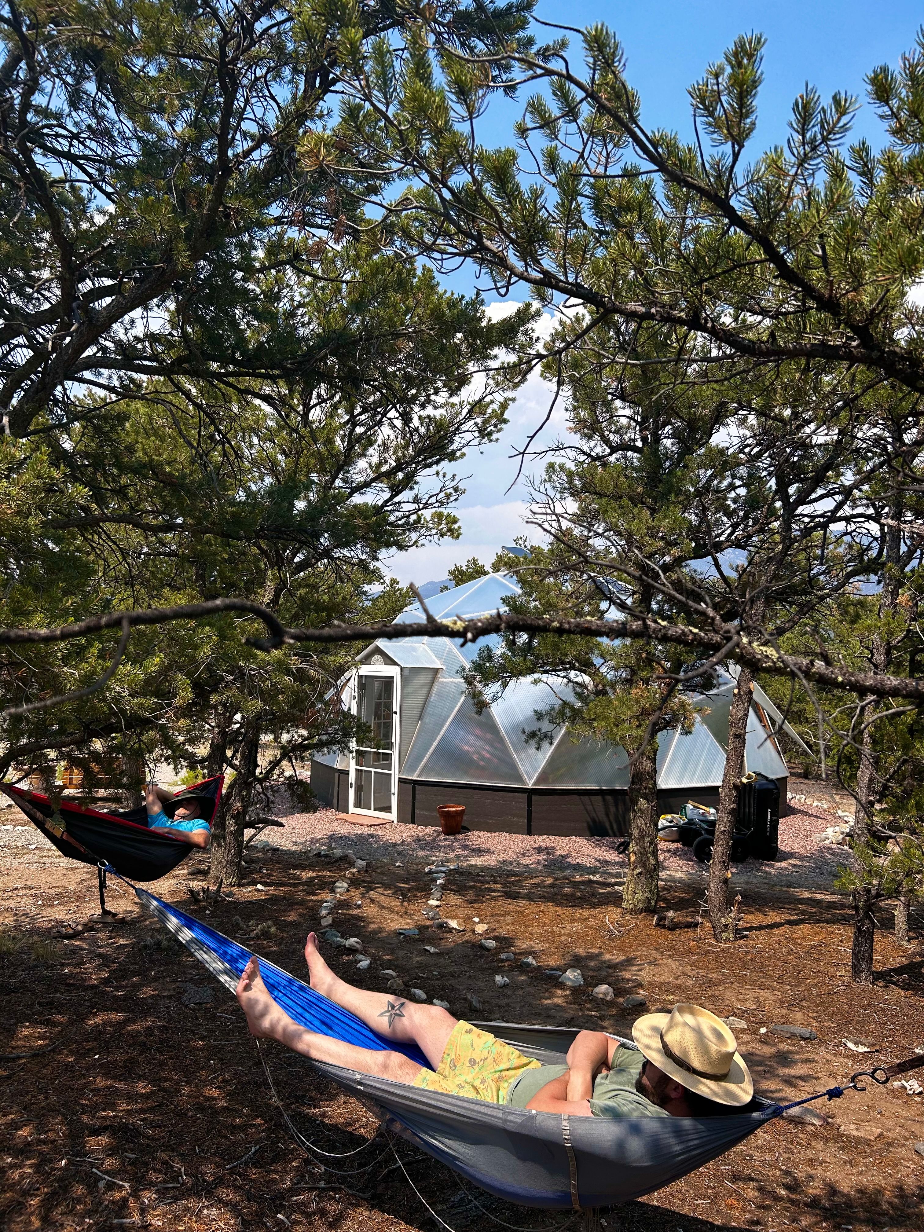 Two people resting in hammocks outside of their Growing Dome greenhouse