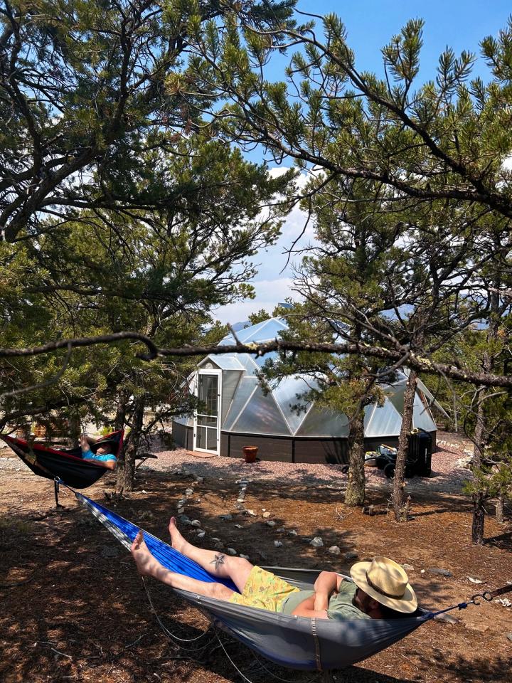 Two people resting in hammocks outside of their Growing Dome greenhouse