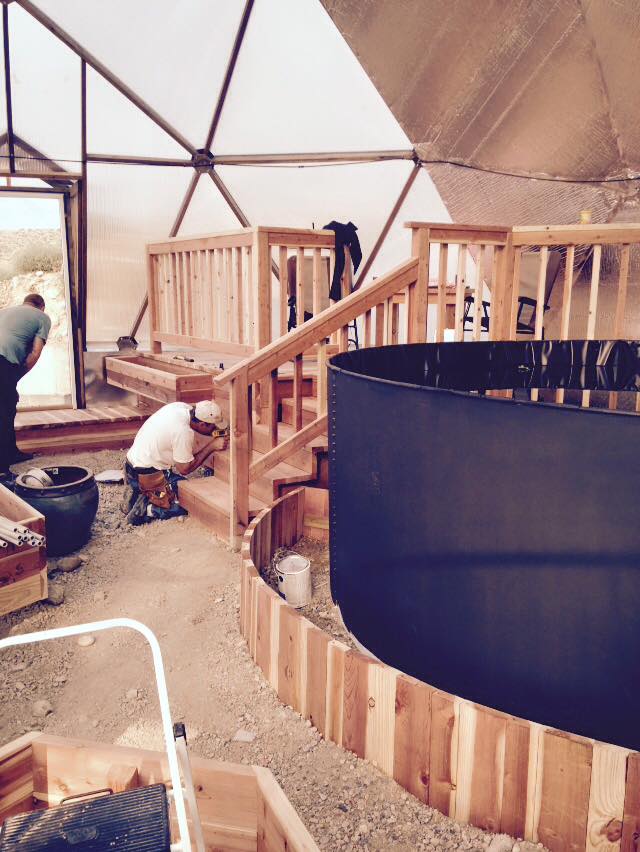 installers finish a deck and custom beds around the pond inside the growing dome greenhouse