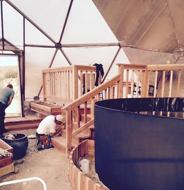installers finish a deck and custom beds around the pond inside the growing dome greenhouse