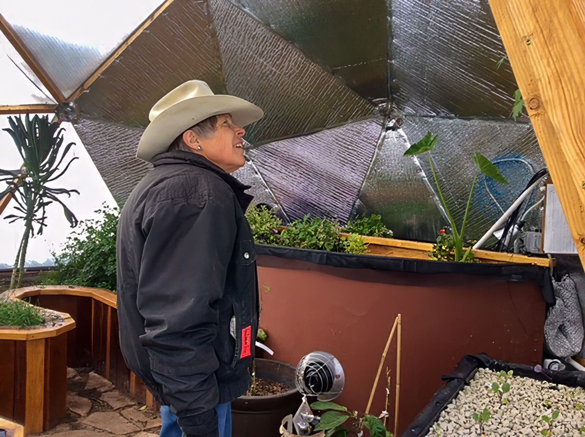 woman in a cowboy hat checking out the inside of a growing dome greenhouse