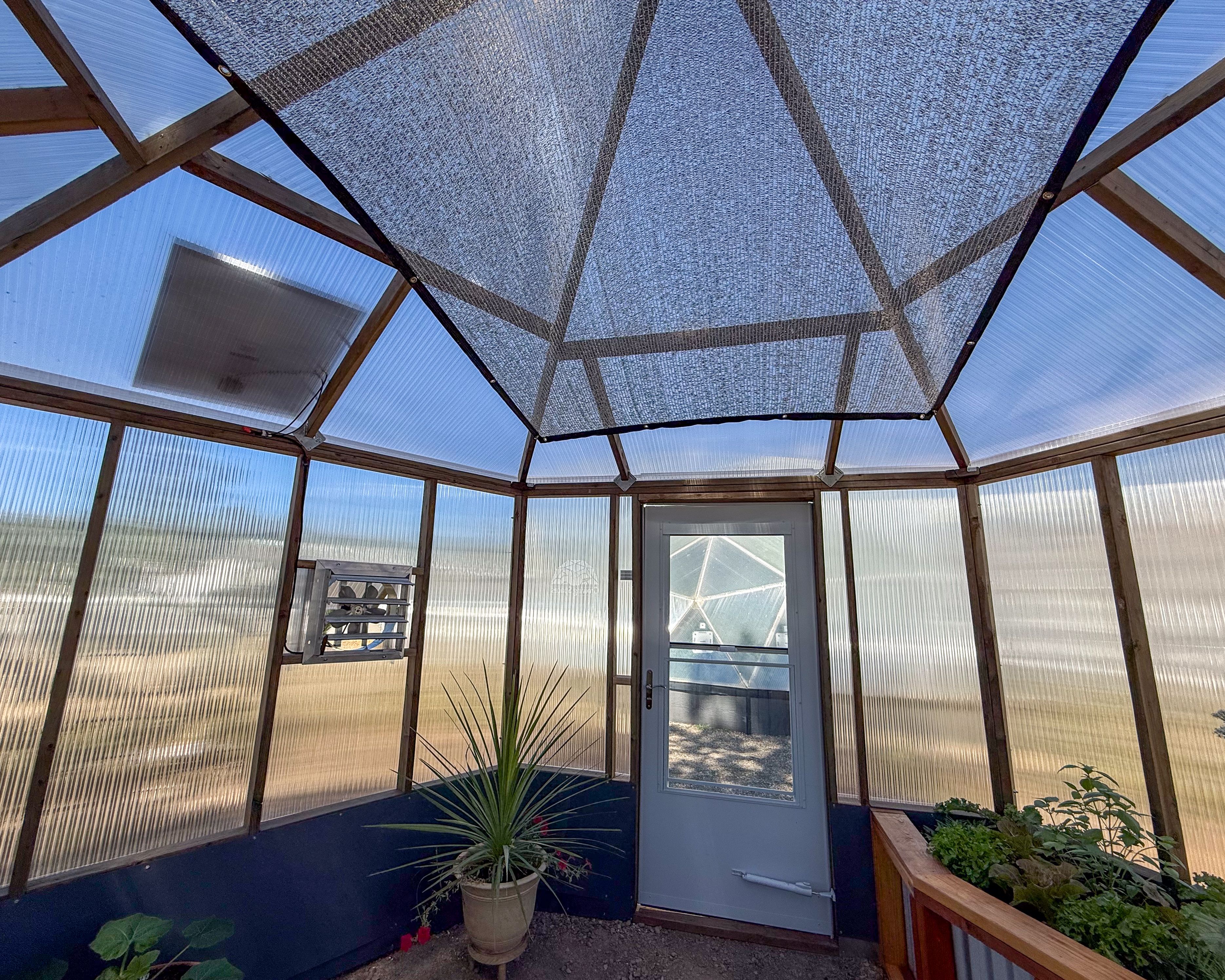 greenhouse interior featuring a solar powered fan, aluminet shade cloth, and raised garden beds