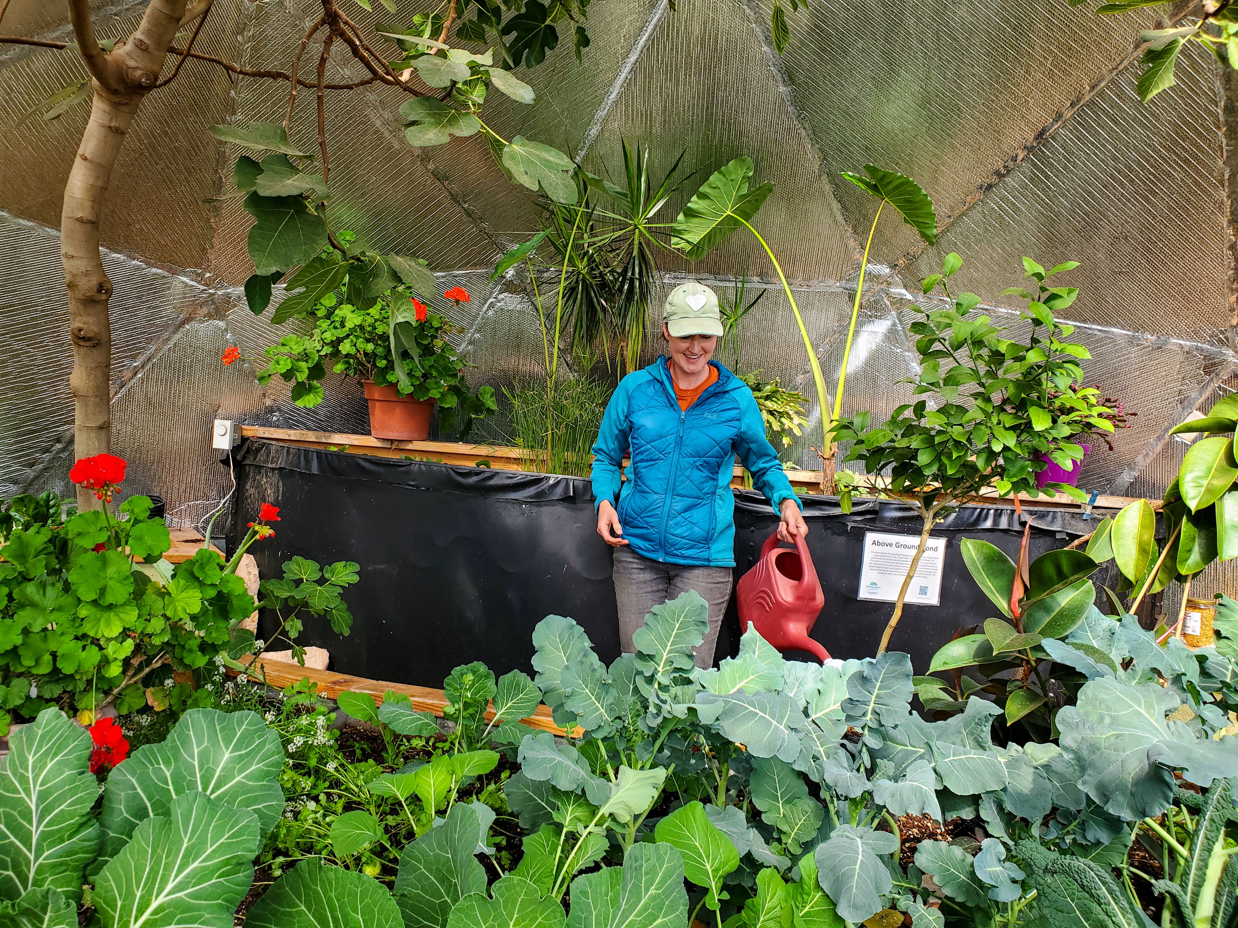 Woman smiling while watering winter crops in front of a pond in a greenhouse