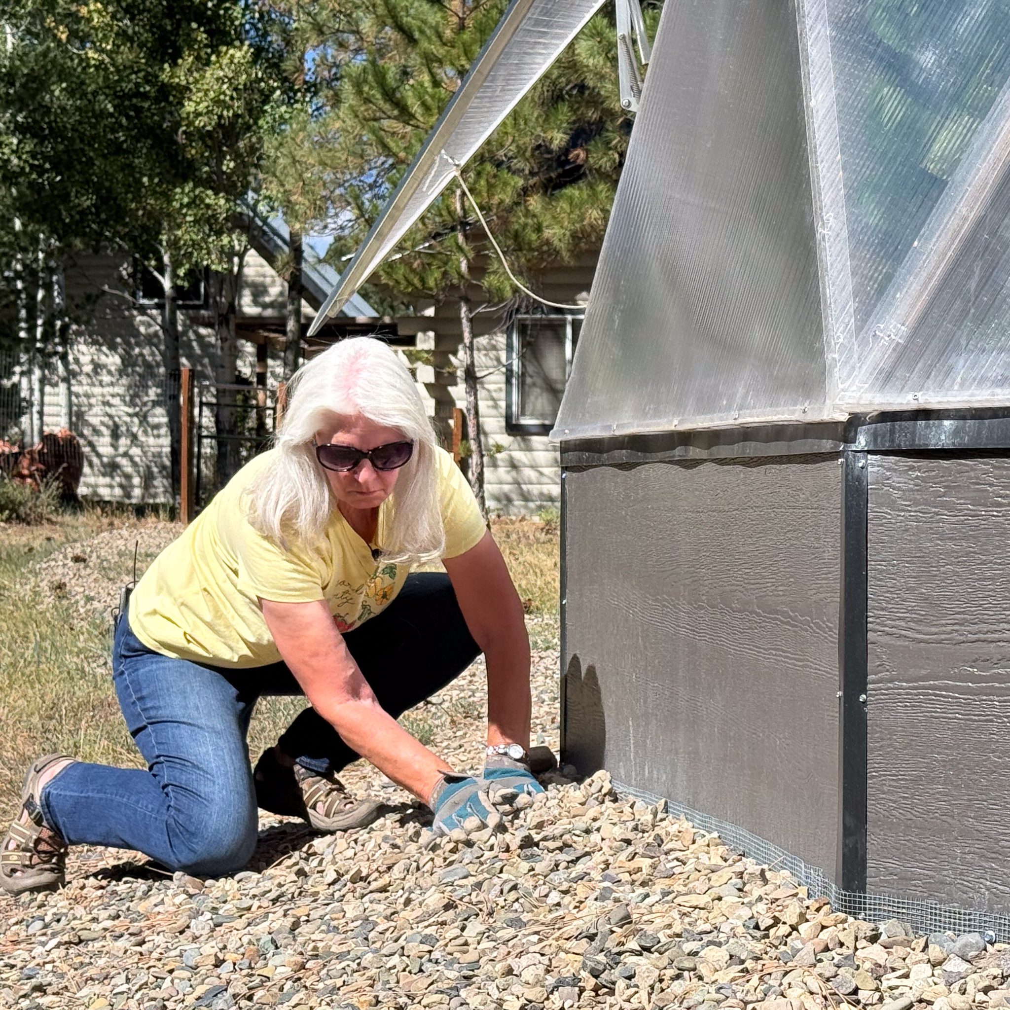 Grower covering hardware cloth with gravel along the base of a Growing Dome on a Colorado meadow
