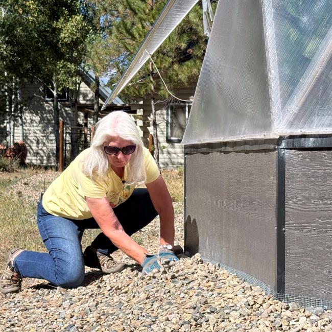 Grower covering hardware cloth with gravel along the base of a Growing Dome on a Colorado meadow