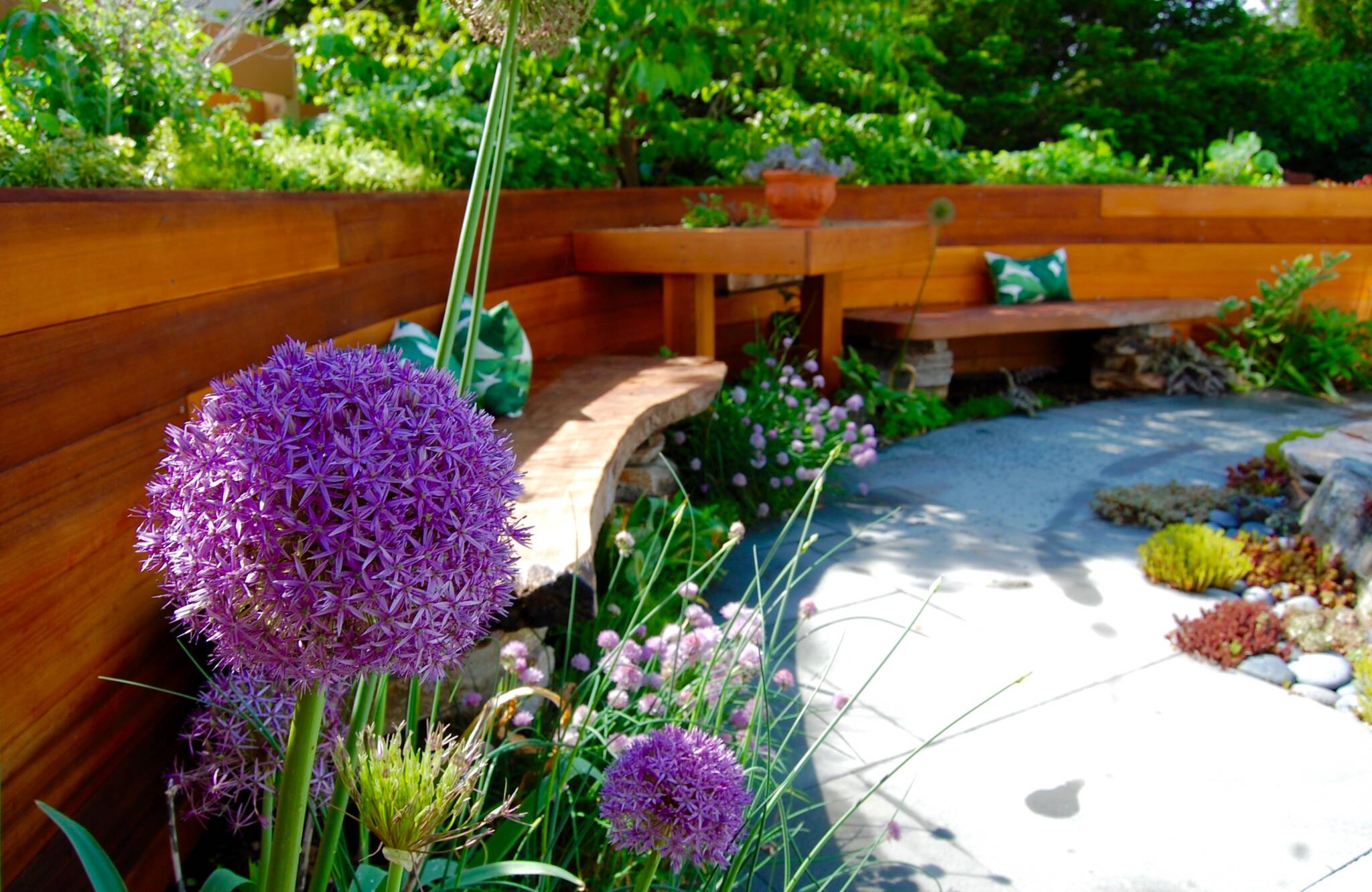 Curving cedar raised bed, growing edible plants, built around garden sculptures, a water feature, and nestled next to a flowering dogwood tree