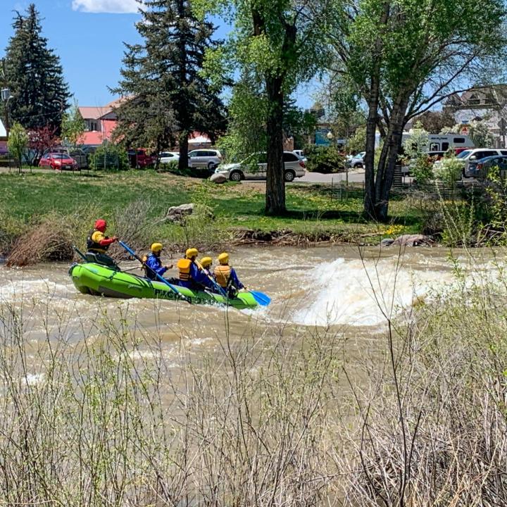 Green raft with 5 people going through a rapid in the heart of downtown Pagosa Springs